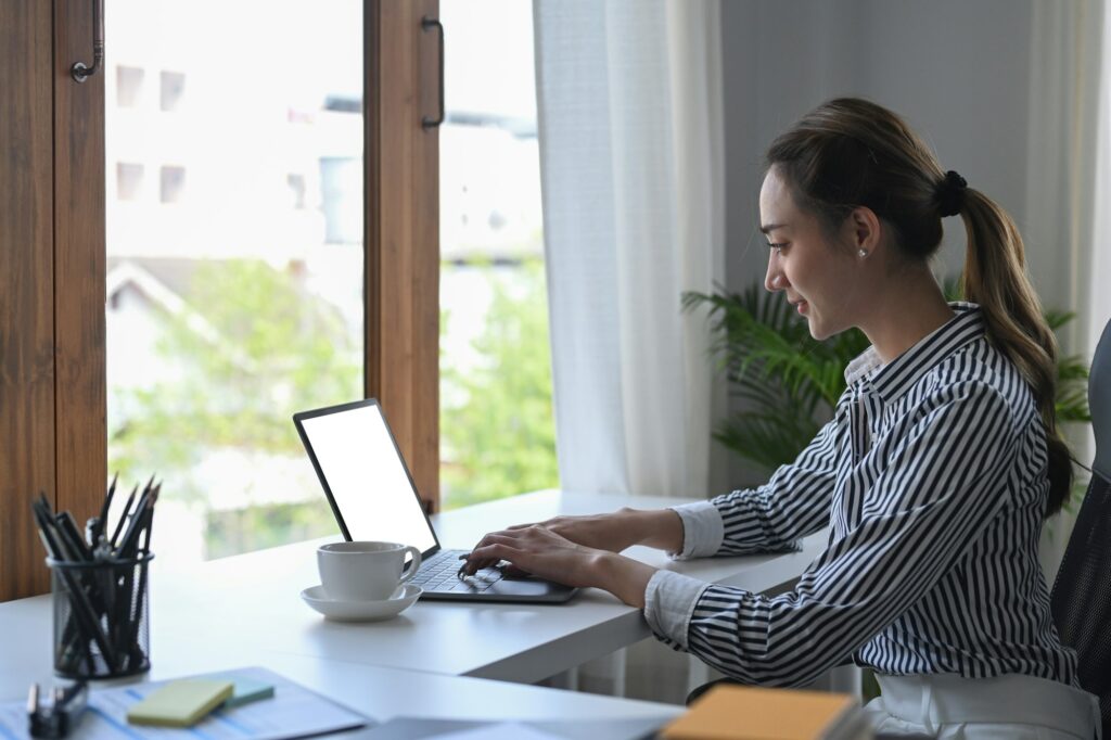 Side view focused female office worker working with laptop computer in bright office.